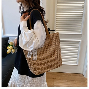 Detail of large straw tote bag featuring a woven texture and white lace bow decoration