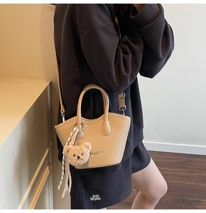 Détail du sac seau beige avec pendentif ours et foulard rayé sur la poignée main