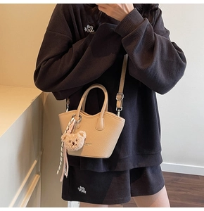 Détail d'un sac seau beige avec un charm d'ours en peluche et un ruban rayé élégant