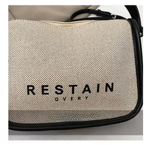 Detail of canvas shoulder bag with black leather trim and RESTAIN letter print