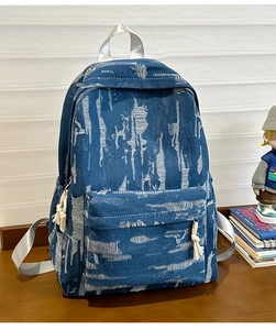 Macro detail of blue denim backpack showing distressed texture and white fringe tassels