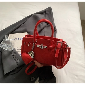 Dettaglio borsa in pelle rossa con trama litchi, chiusura a girello e ciondolo a cuore