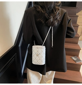 Détail du sac seau blanc matelassé avec clous argentés et pendentif étoile sur blazer