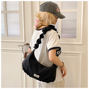 Detail einer schwarzen Hobo-Tasche aus Nylon mit modischem Rüschen-Schultergurt am Modell