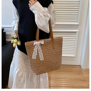 Close-up of straw woven tote bag with a white lace bow and brown leather handles