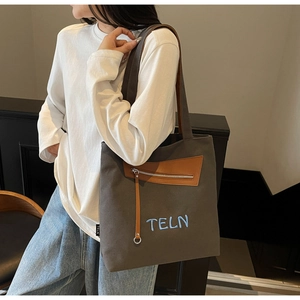Détail du cabas en toile grise avec poche en cuir marron et broderie TELN bleue