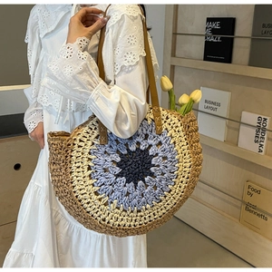 Detail of round straw beach bag with blue concentric crochet pattern and brown leather handles