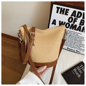 Detail of woven straw bucket bag with brown leather base and adjustable shoulder strap