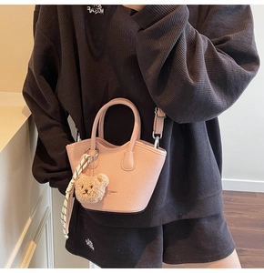 Détail du sac seau rose en cuir grainé avec un pendentif ours et un ruban rayé