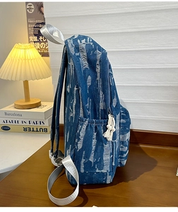 Close-up of distressed blue denim backpack with white frayed details and fringe tassel