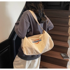 Détail d'un grand sac bandoulière en toile crème montrant la broderie et la capacité