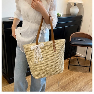 Close-up of beige straw tote bag featuring brown leather handles and delicate lace bow detail