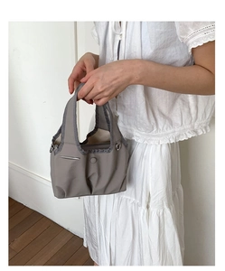 Detail of gray nylon handbag showing side metal D-rings and minimalist button accent