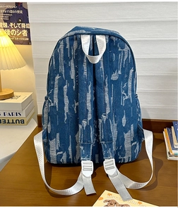 Detailed view of distressed denim backpack with white woven straps on a warm cozy desk