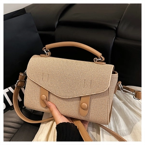 Detail of a beige straw tote bag with camel leather flap and round decorative buckles
