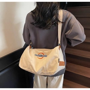 Vue détaillée d'un sac bandoulière minimaliste en toile crème avec broderie du logo bleu