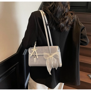 Detail of silver shoulder bag with wood grain texture and large mesh bow on a model