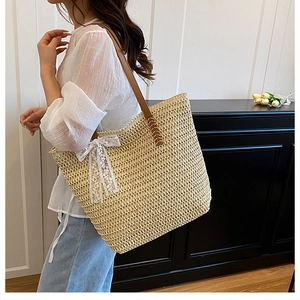 Detail of large straw tote bag with brown leather straps and a white lace bow accent
