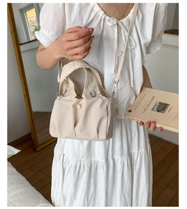 Detail of a minimalist cream-colored crossbody bag with adjustable strap and top handle