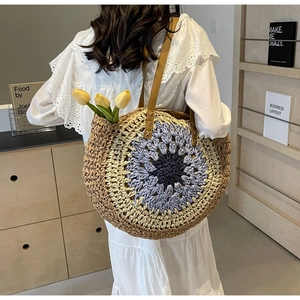 Detail view of round woven straw beach bag with floral pattern and leather straps
