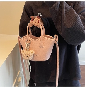 Petit sac seau rose grainé avec breloque ours porté en bandoulière par un modèle