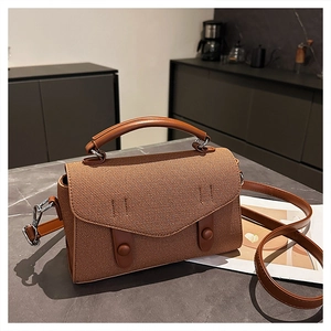 Detail of a brown textured crossbody bag with silver hardware on marble surface