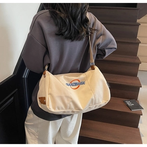 Détail d'un sac bandoulière en toile crème avec broderie bleue porté par un mannequin
