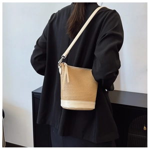 Close-up of straw bucket bag with cream leather accents worn over a black blazer