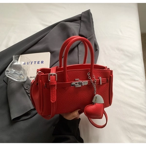 Dettaglio borsa a mano in pelle rossa con chiusura a scatto e ciondolo a cuore