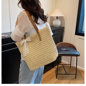 Detail of hand-woven straw tote bag featuring leather straps and a delicate lace bow