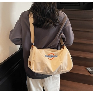 Détail du sac bandoulière en toile beige avec finitions en cuir et logo brodé