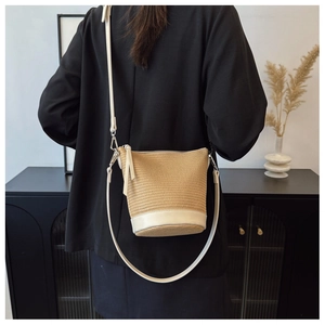 Detail of hand-woven beige straw bucket bag with adjustable leather strap on a model