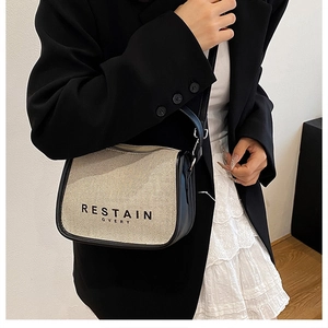 Detailed close-up of the beige canvas and black leather crossbody bag with text logo