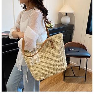 Detail of straw tote bag featuring brown leather handles and a delicate white lace bow accent