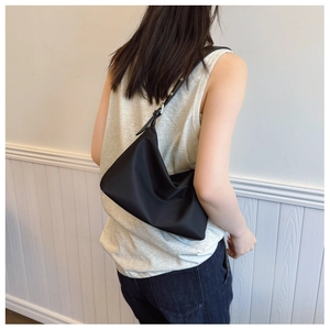 Minimalist black nylon hobo bag shown on shoulder with adjustable leather strap