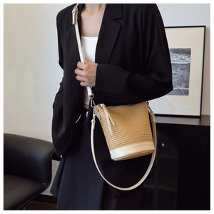 Straw bucket bag detail with white leather trim and adjustable shoulder strap on model