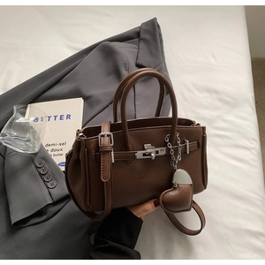 Dettaglio borsa in pelle marrone caffè con trama litchi, chiusura argento e ciondolo