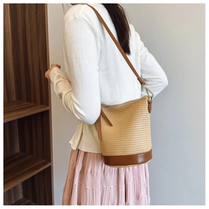 Detail of woven straw bucket bag with brown leather base and strap on model