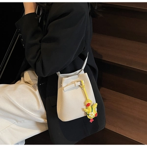 Detailed view of white lychee leather bucket bag featuring a cute yellow duck pendant