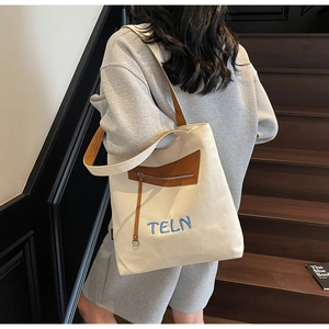 Détail du sac cabas en toile beige avec finitions cuir brun et broderie TELN bleue