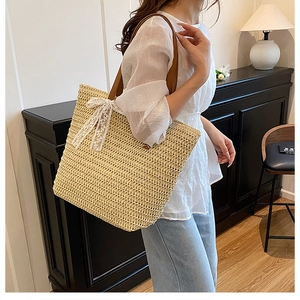 Straw tote bag detail with brown leather strap and elegant white lace bow decoration