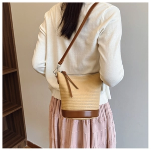 Detail of straw bucket bag with brown leather trim and tassel zipper on a white sweater
