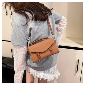 Close-up of textured brown crossbody bag with dual decorative buttons and top handle