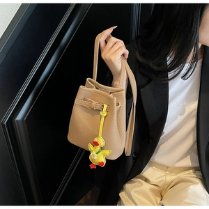 Detailed view of cream bucket bag with lychee texture and yellow duck charm