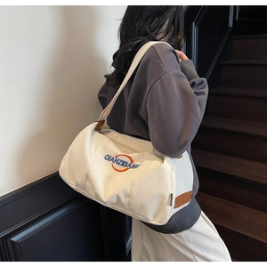 Mannequin portant un grand sac bandoulière en toile crème avec lettrage bleu et finitions cuir