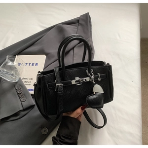 Dettaglio borsa a mano nera in pelle a grana con hardware argento e ciondolo a cuore su giacca