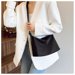 Detail of minimalist black tote bag with adjustable leather strap worn by a model