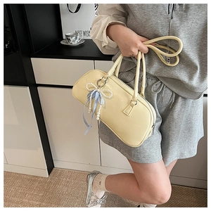 Dettaglio di una borsa Boston giallo crema con ciondolo a fiocco di perle e manici lunghi
