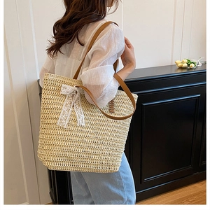 Detail of woven straw tote bag featuring white lace bow and brown leather shoulder straps