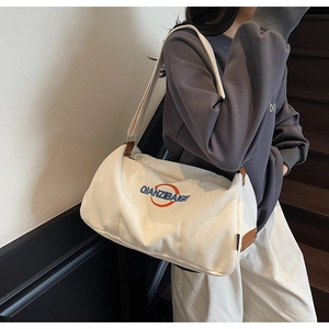 Détail du sac polochon en toile blanche avec lettrage et accents en cuir marron